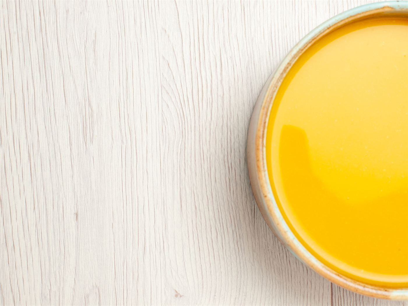 A bowl of golden homemade ghee on a whitewashed wooden table